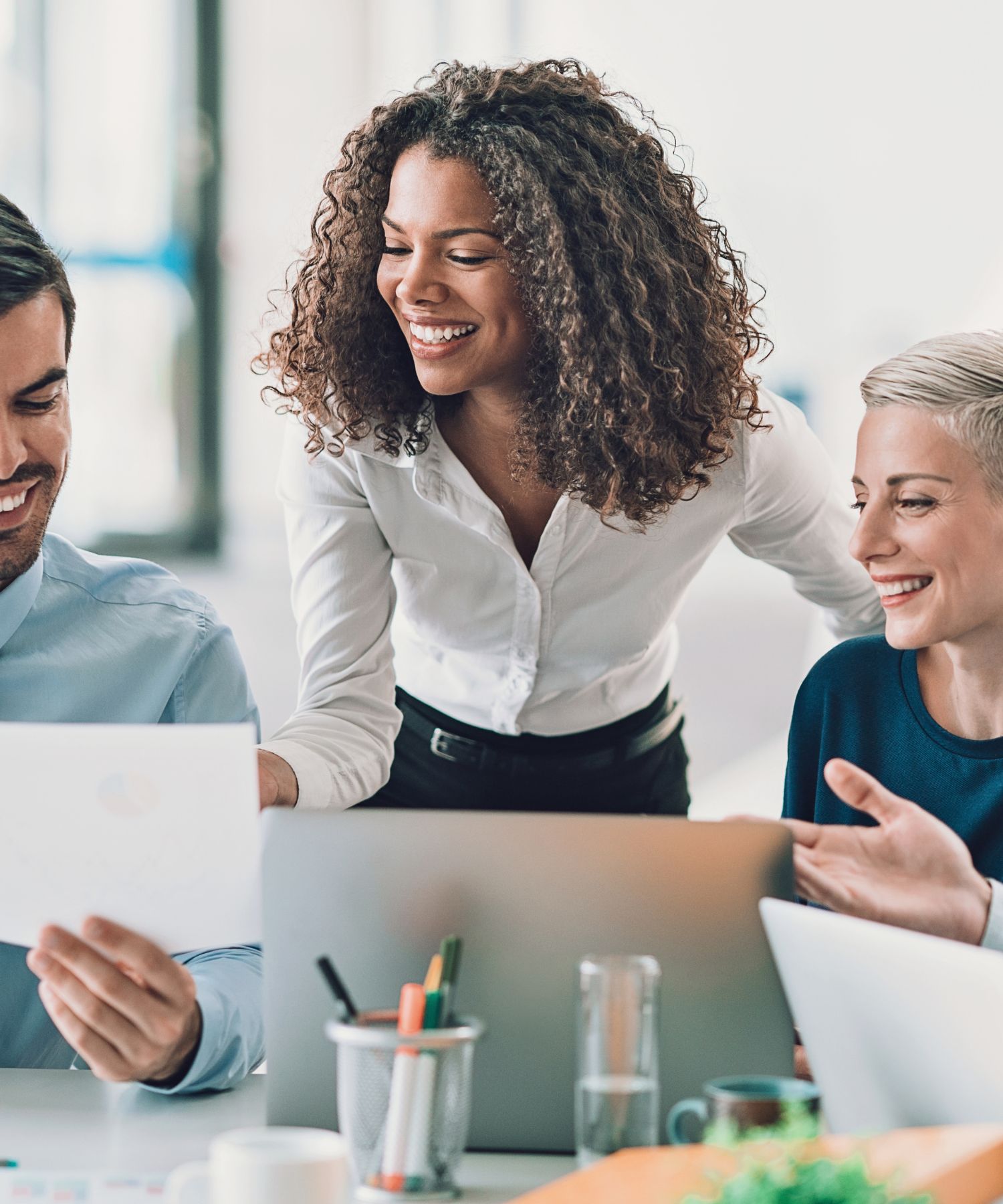 african american woman smiling and leaning over table with laptop talking to team members